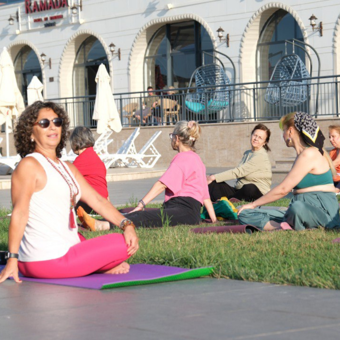 Figen Tekkol, açık havada çimler üzerinde bir grup katılımcıya fasya odaklı yoga dersi verirken.